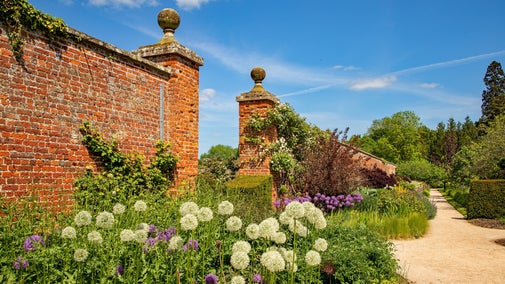 The red stone walls and entranceway to the Walled Garden at Wimpole Estate stand above beds of summer flowers